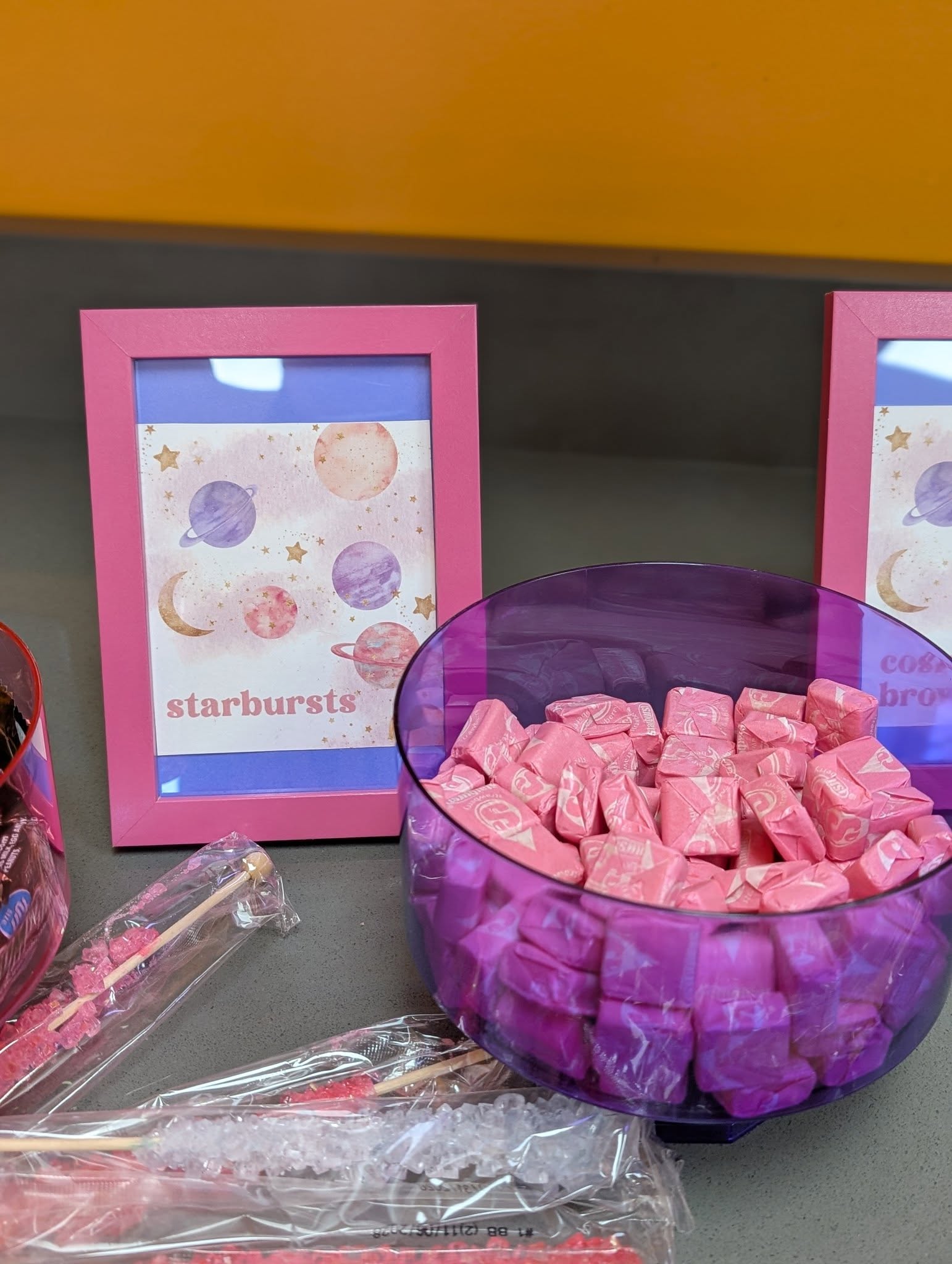 Pink bowl filled with pink Starburst candies next to a framed space-themed sign.
