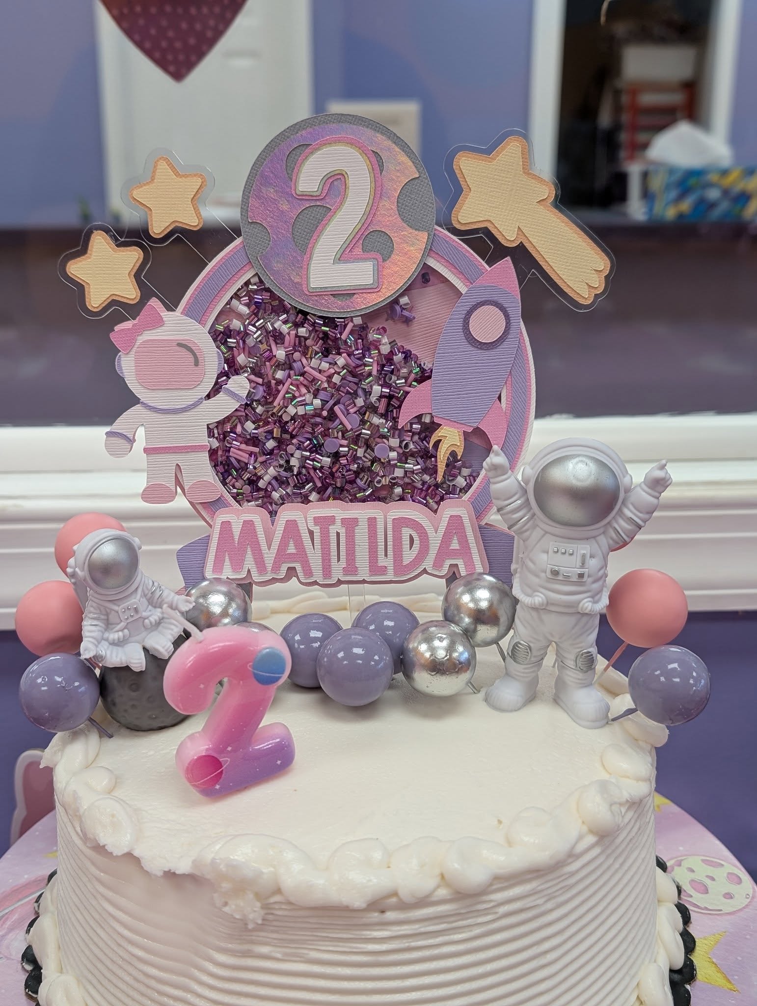Custom space-themed second birthday cake topper with glitter, astronaut figures, and the name Matilda.