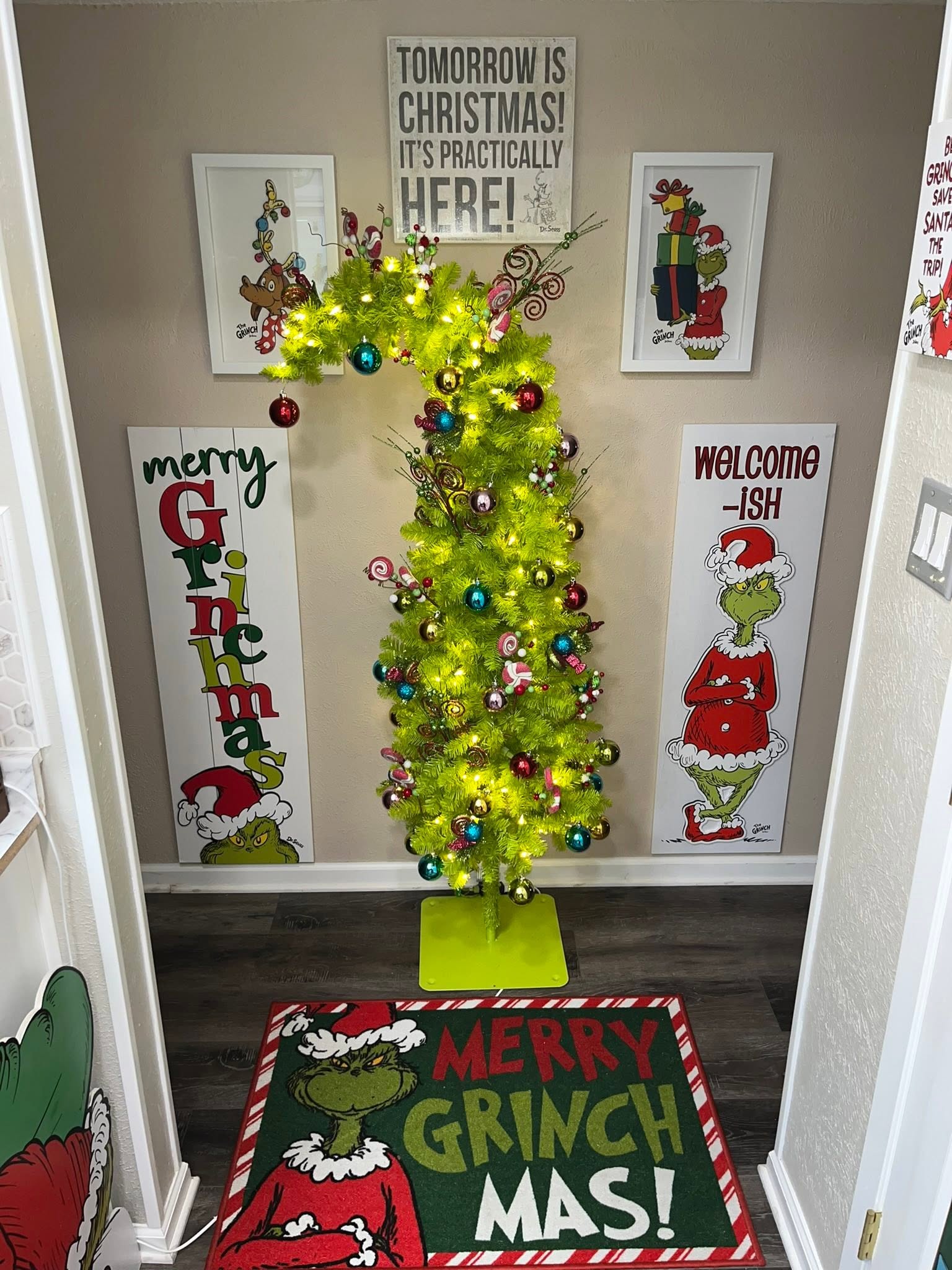 A lime green Grinch-themed Christmas tree with ornaments and decorations in a room decorated with Grinch signage.