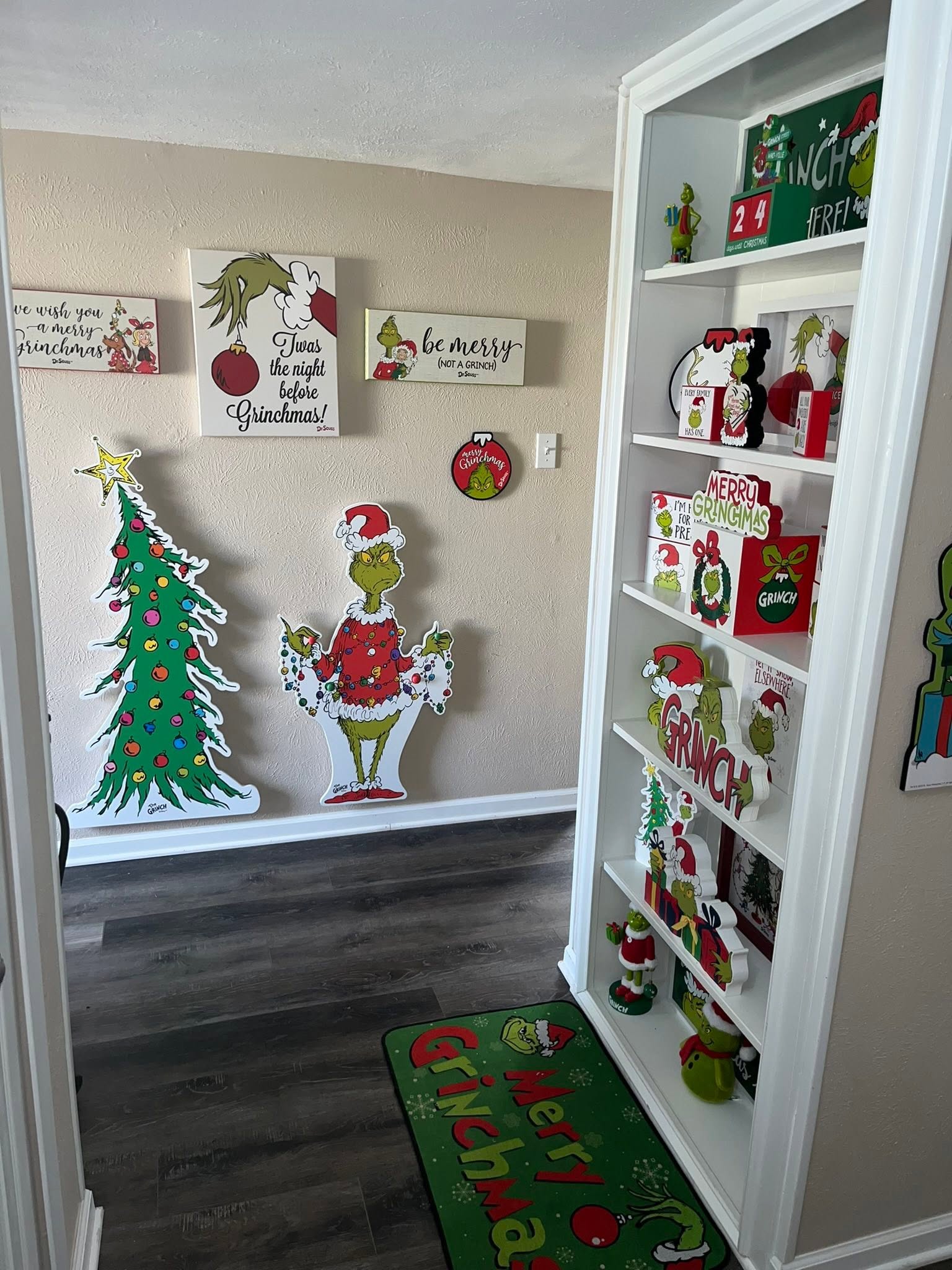 Room decorated with Dr. Seuss The Grinch Christmas wall art, large floor cutouts, and a shelving unit filled with Grinch holiday decor.