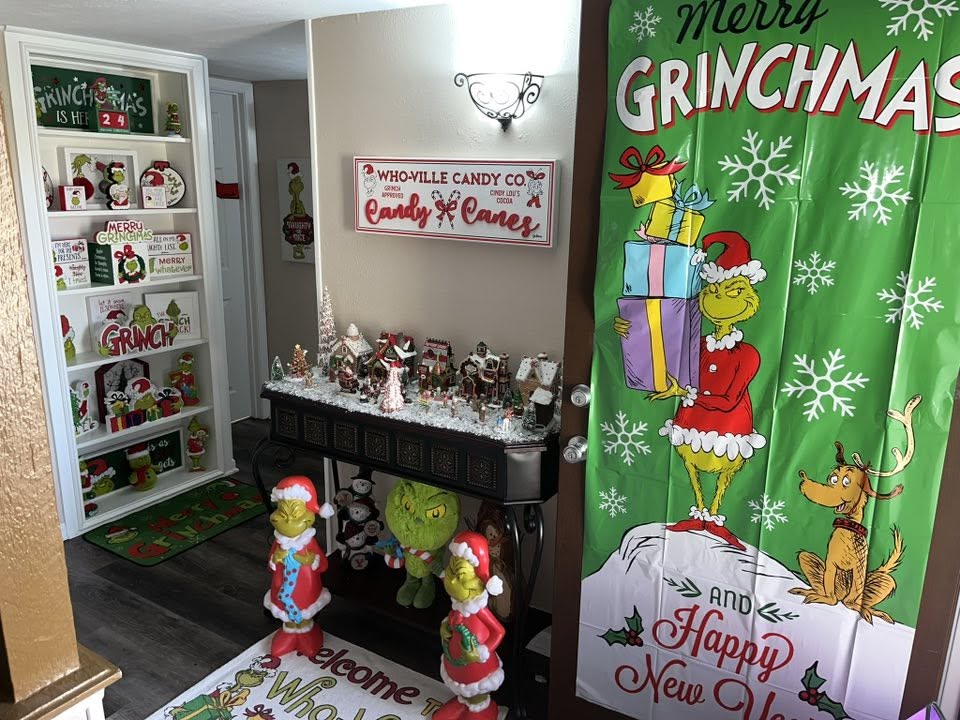 Indoor home decor featuring multiple Grinch-themed Christmas signs, figures, and a large hanging Grinch Christmas banner.