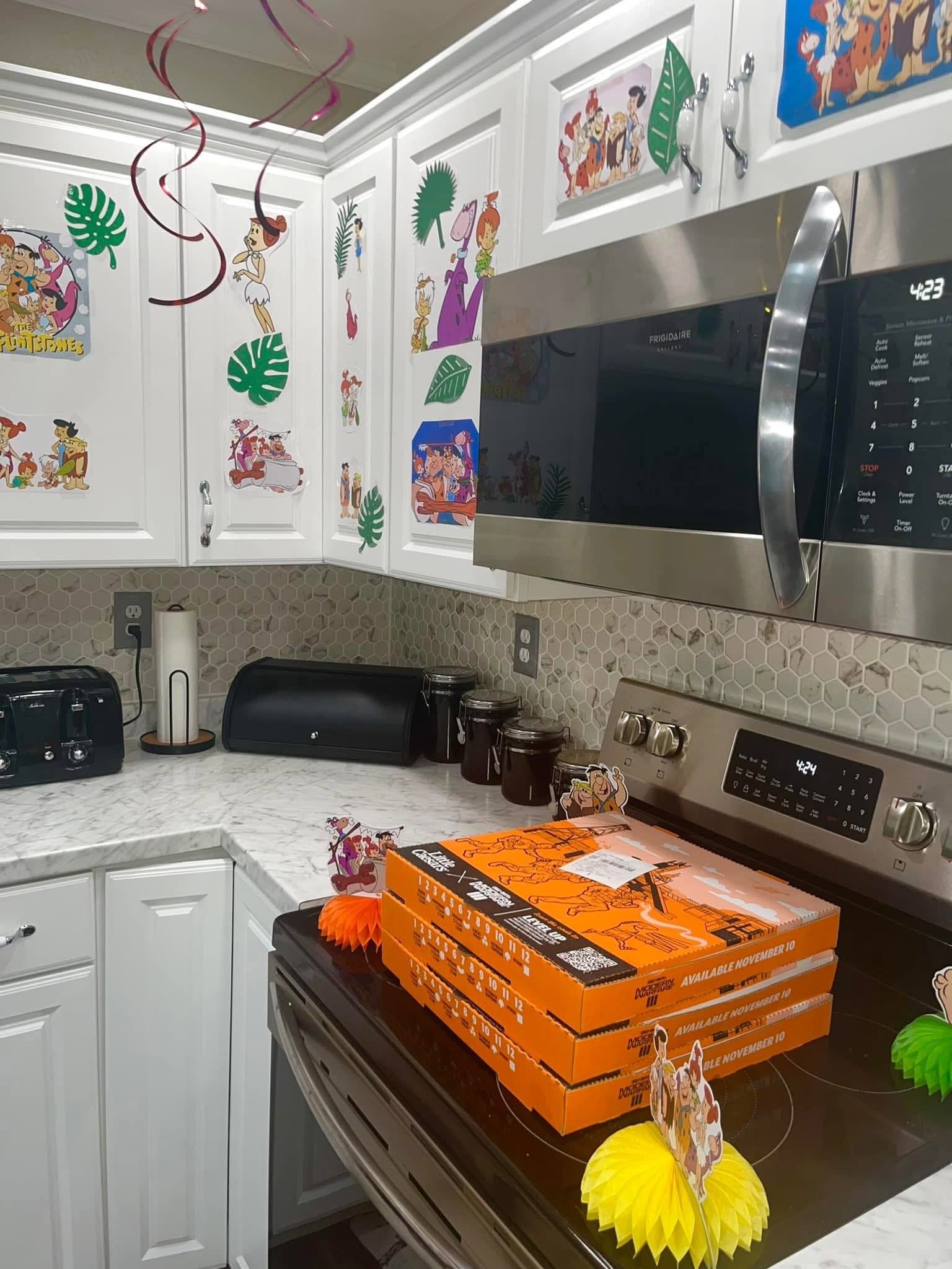 Kitchen decorated with The Flintstones cutouts and stacks of Little Caesars pizza boxes on the stove