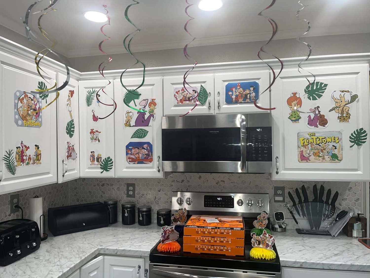 Kitchen cabinets and stove decorated with The Flintstones themed party cutouts and hanging swirls.