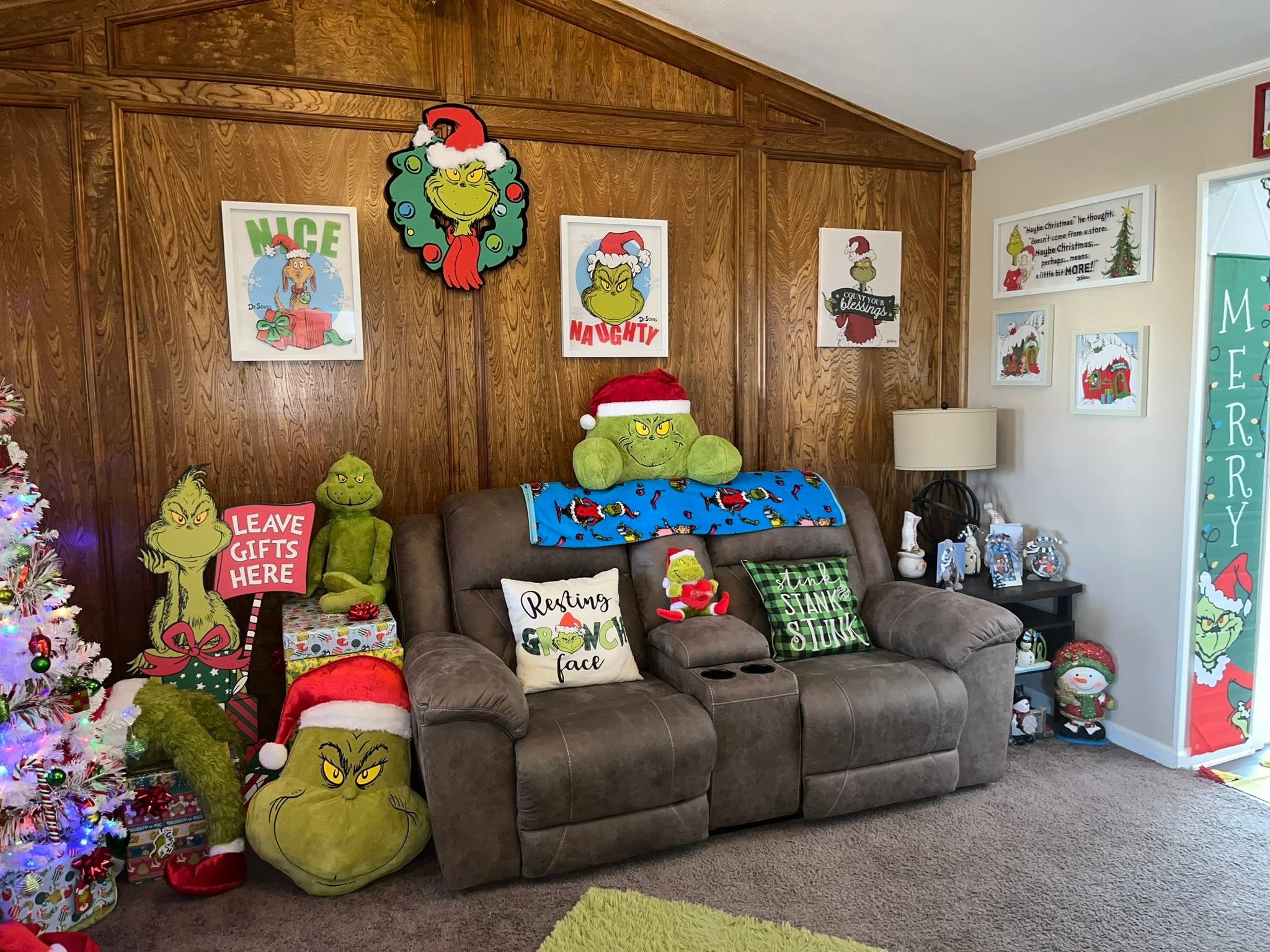 Living room decorated for Christmas with Grinch-themed pillows, wall art, plush toys, and holiday decor.