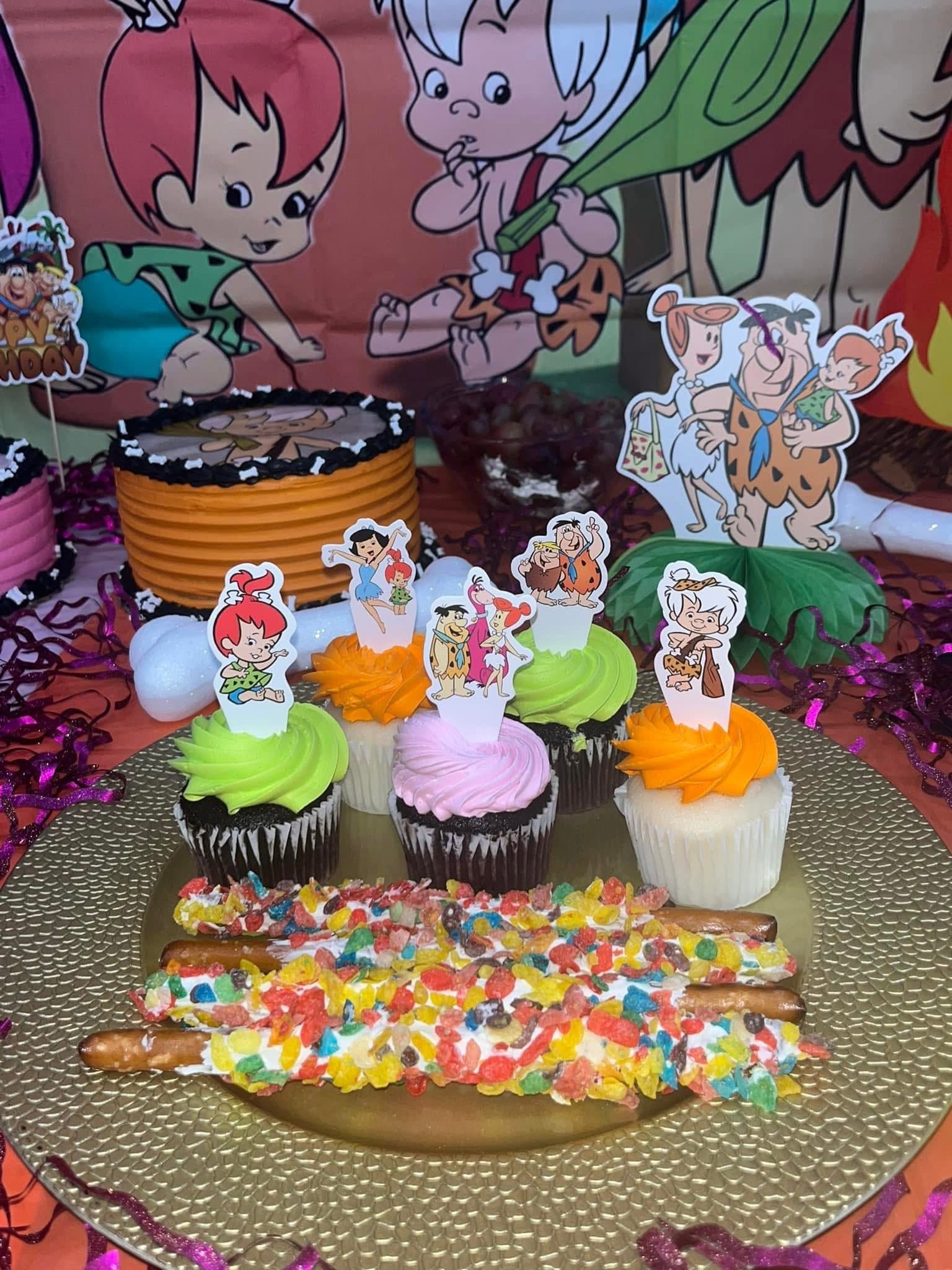 Flintstones themed party setup with cupcakes featuring character toppers and fruity cereal coated pretzel rods.