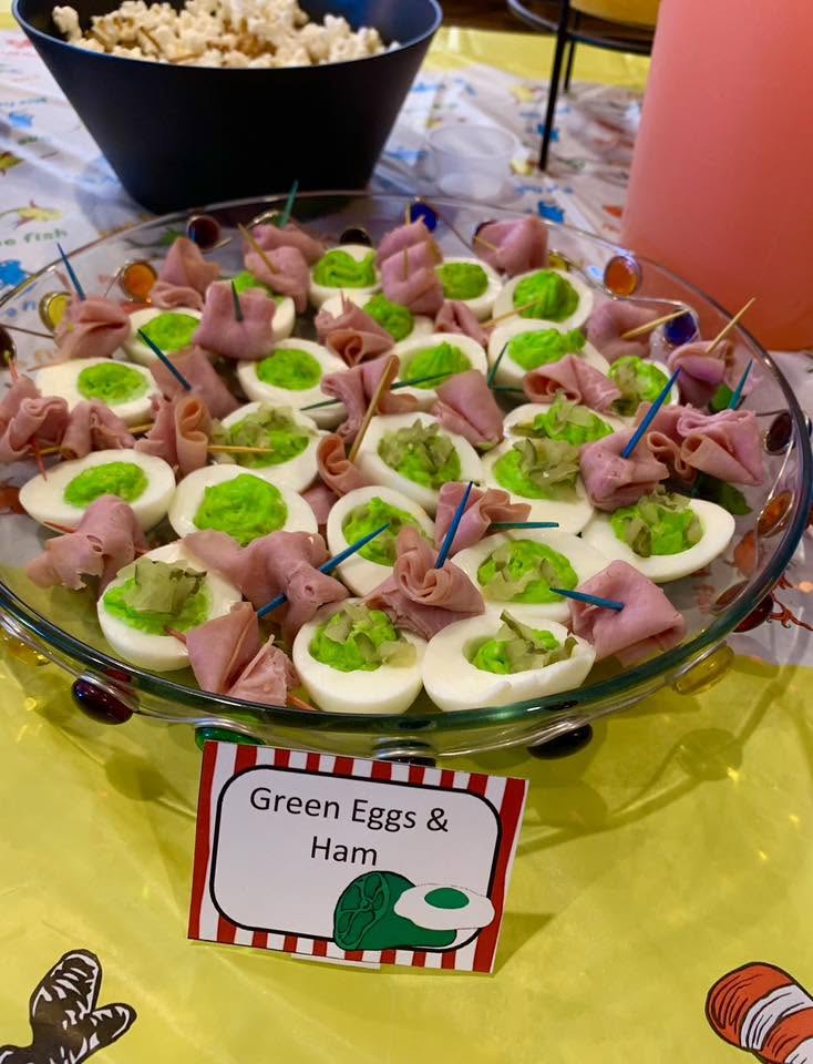 A platter of green deviled eggs garnished with slices of ham, labeled as Green Eggs and Ham for a themed party.
