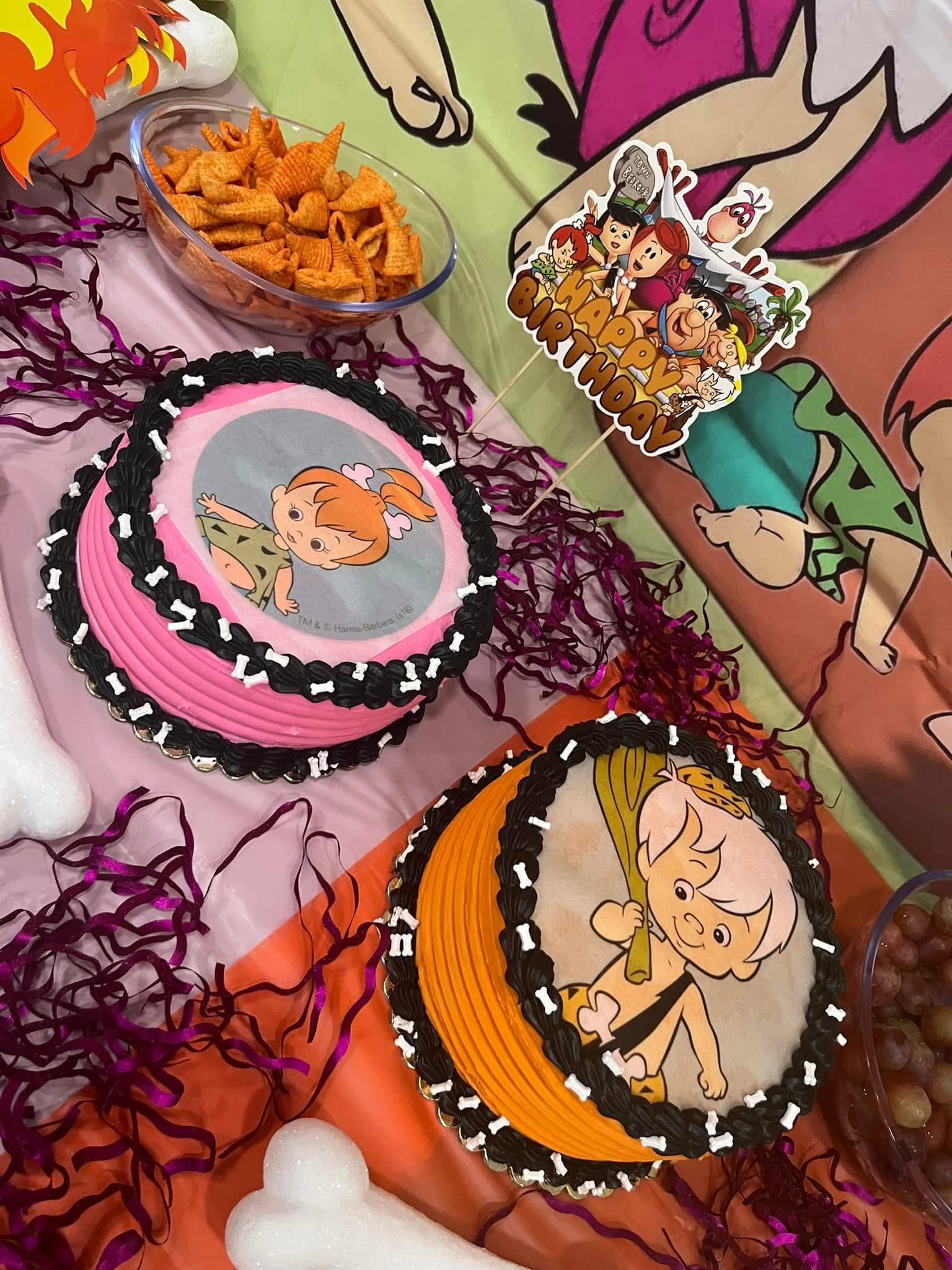 Two round birthday cakes decorated with Flintstones characters Pebbles and Bamm-Bamm and bone-themed icing