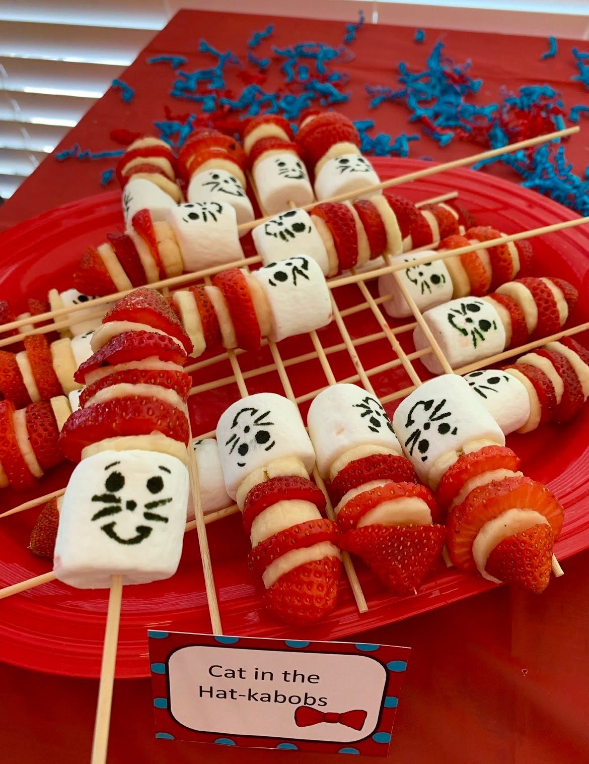 Cat in the Hat-themed fruit kabobs made with marshmallows, strawberries, and bananas served on a red platter.