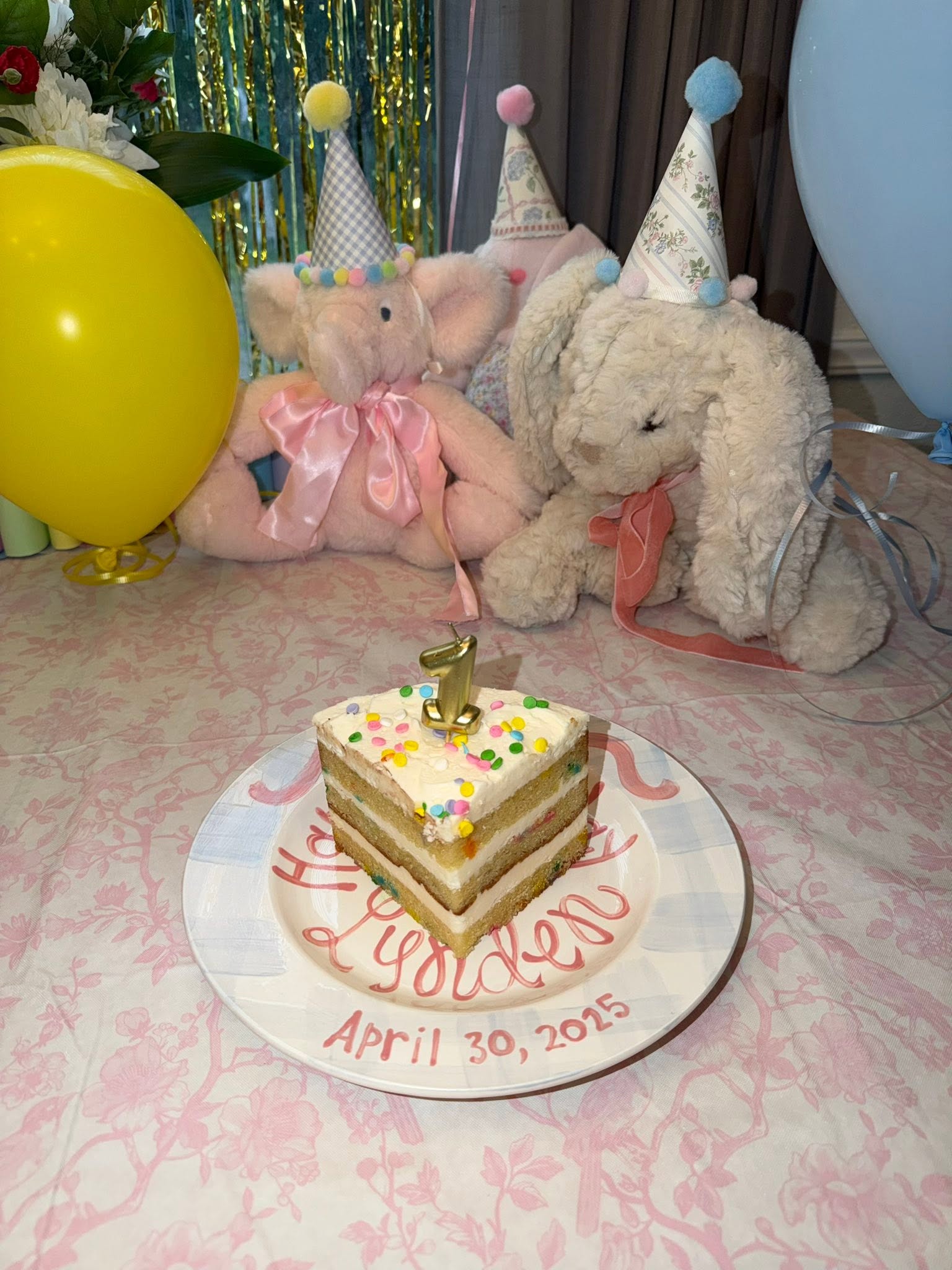 A slice of birthday cake with a number one candle on a plate personalized for Lynden's first birthday.