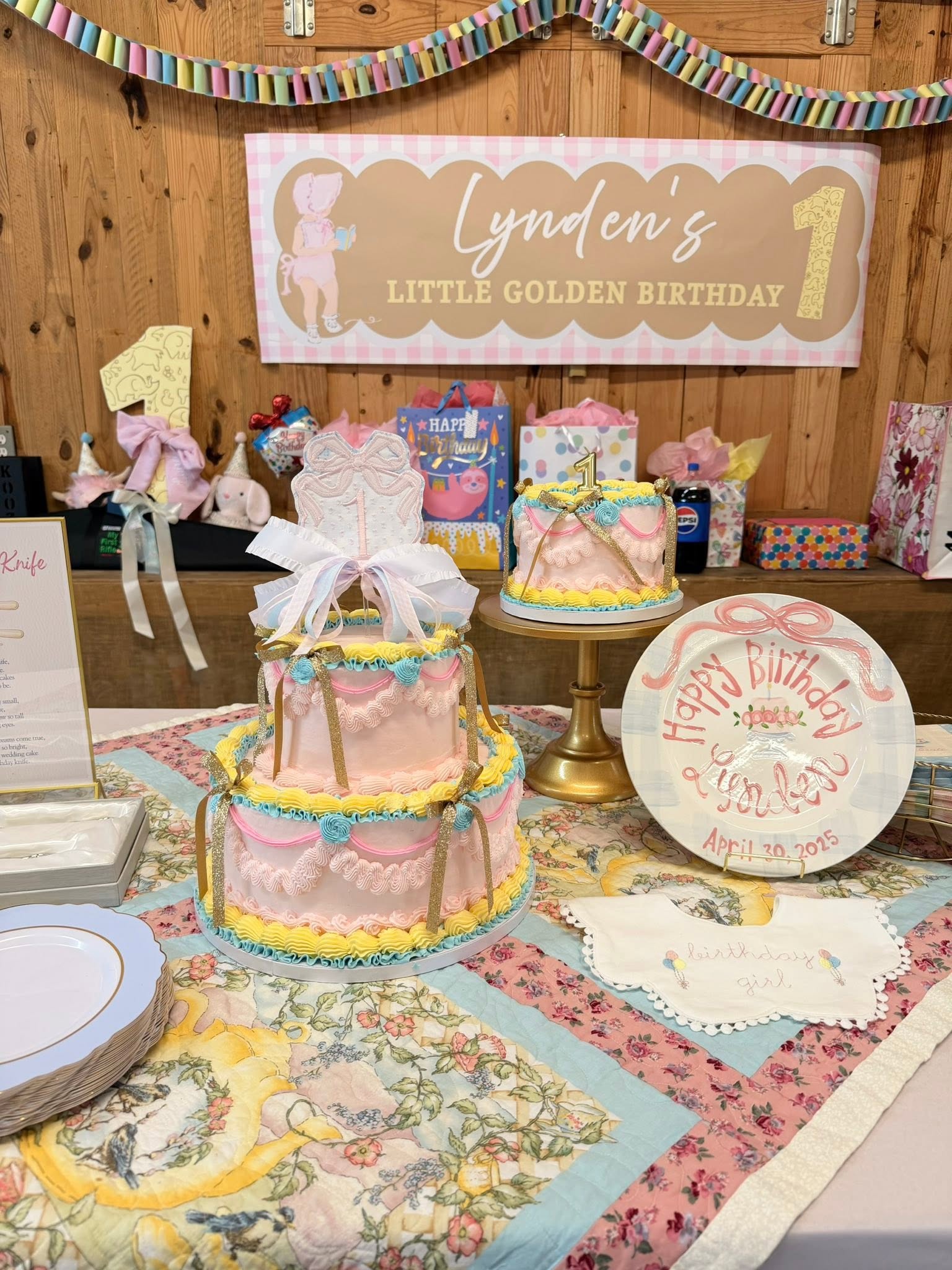 Two-tiered pink birthday cake with yellow frills, gold ribbons, and a number one topper for a first birthday party.