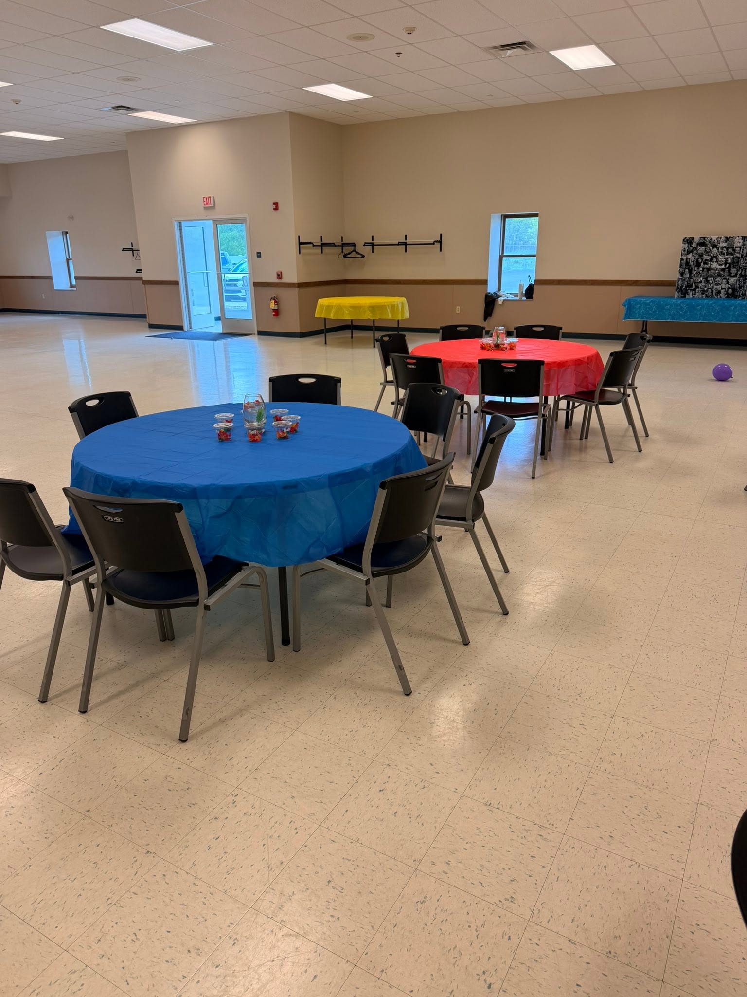 Spacious event hall featuring round tables draped in blue and red tablecloths, set with chairs for a gathering.