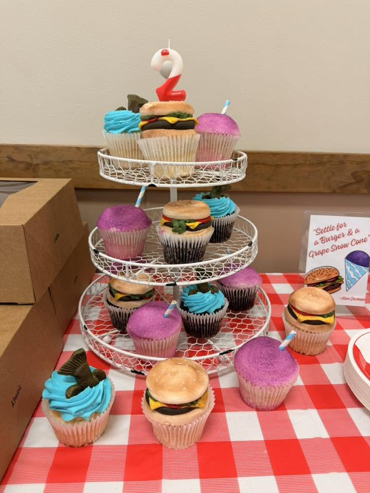 Three-tiered cupcake stand featuring burger-shaped cupcakes and cupcakes with blue and purple frosting.
