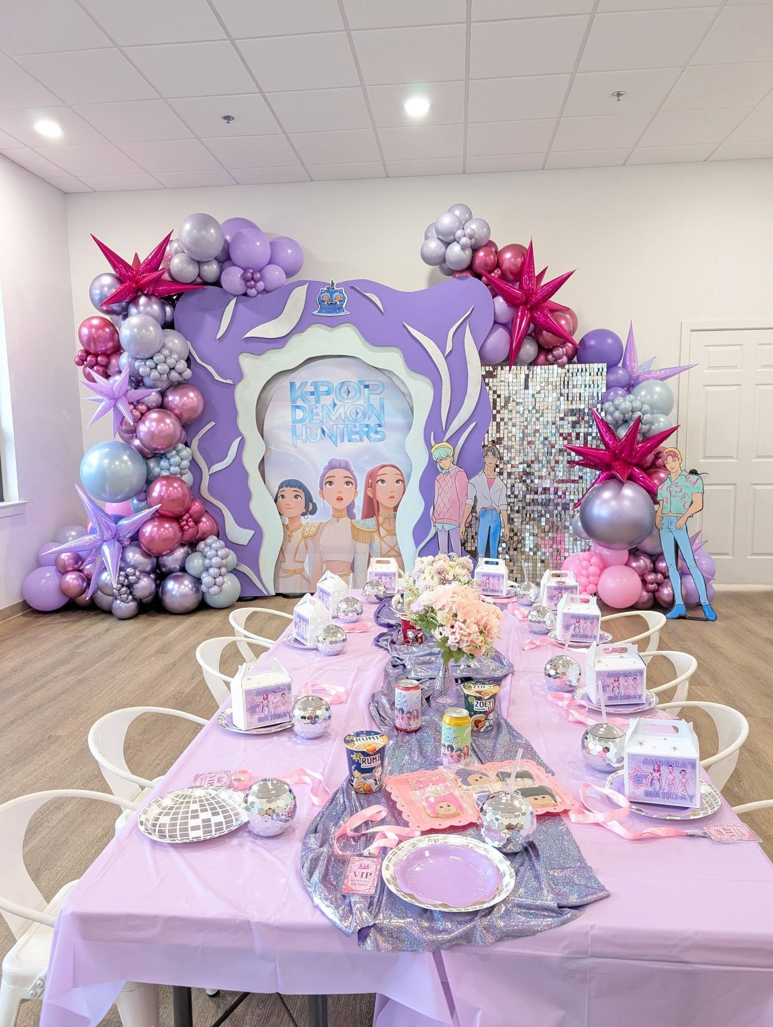 K-pop Demon Hunters themed birthday party setup with purple balloon arch, table decor, and character standees.