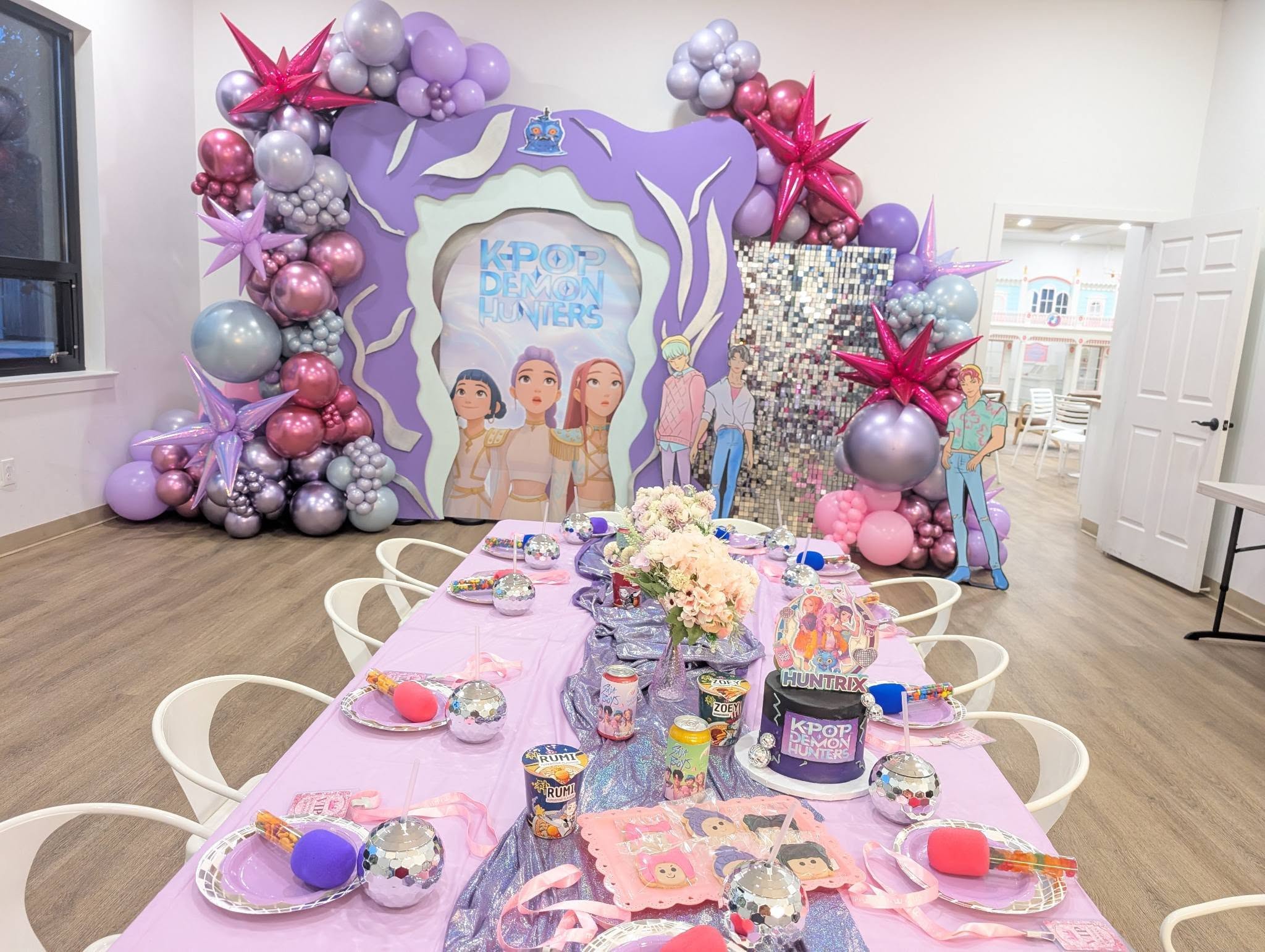 K-pop Demon Hunters themed party table with purple balloon arch, character backdrop, and themed table settings.