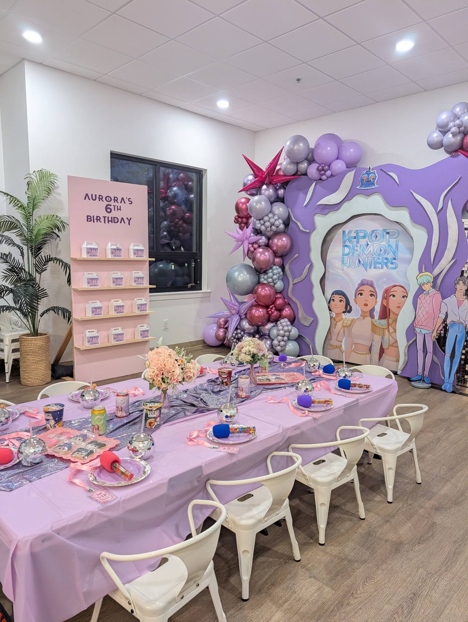 K-pop Demon Hunters themed 6th birthday party setup with a decorated long table, balloon arch, and party favors.