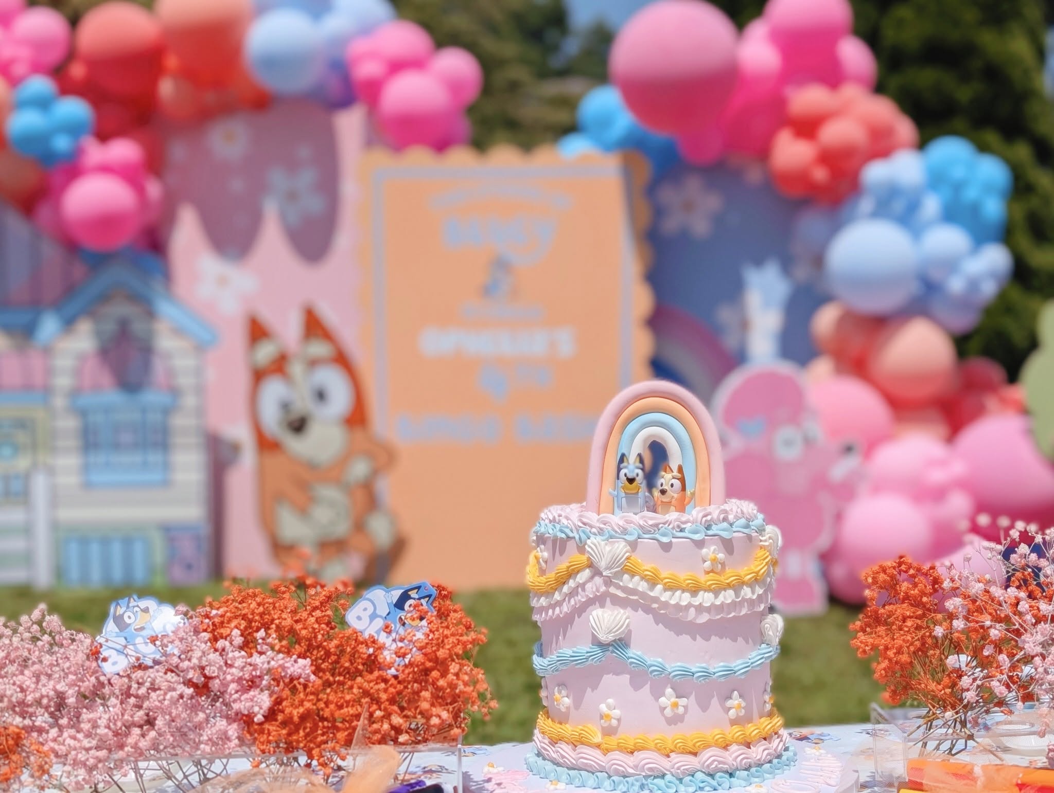 Bluey-themed pink birthday cake topped with a rainbow and miniature Bluey and Bingo figures