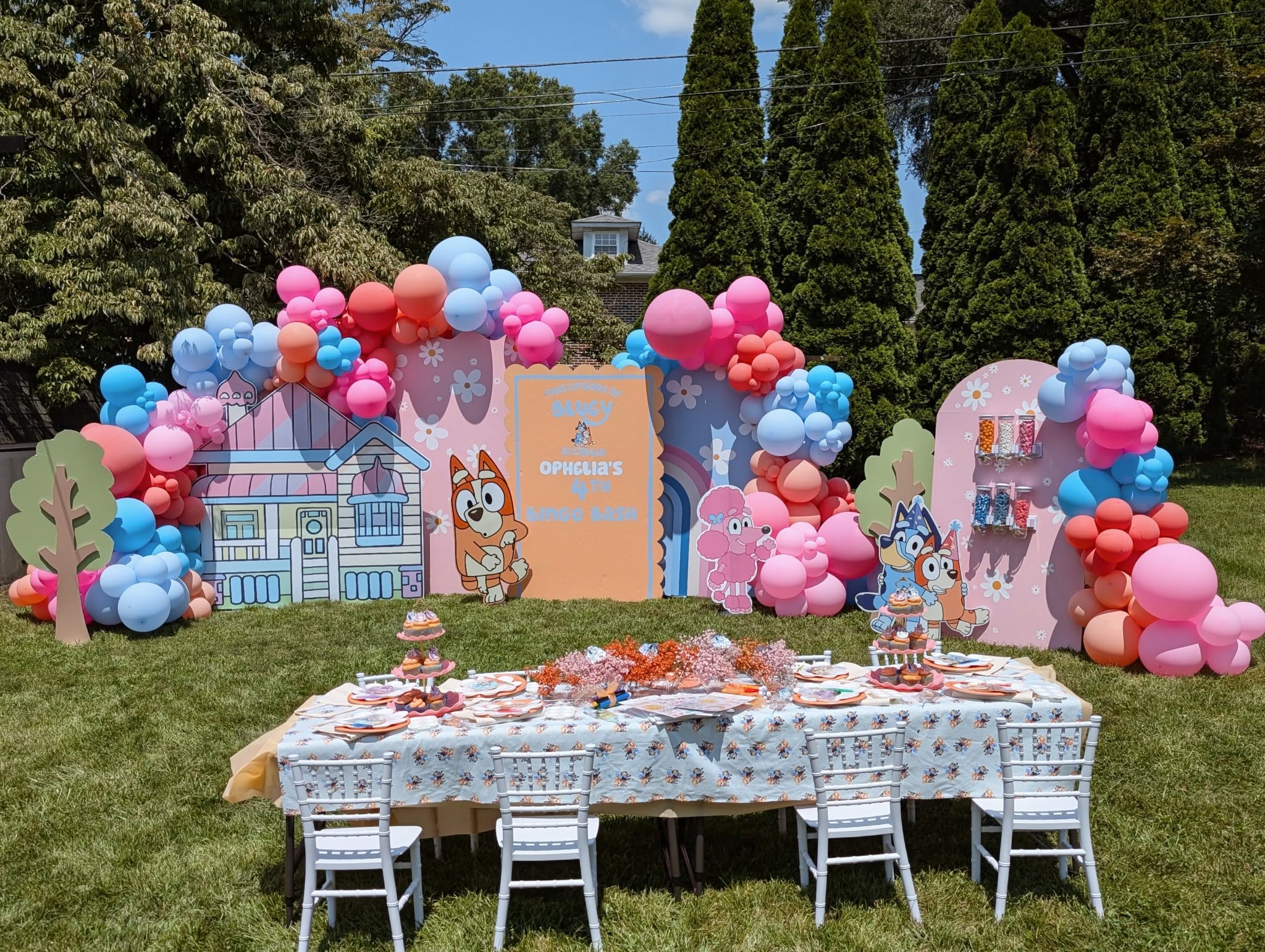 Bluey-themed outdoor birthday party setup with balloon arches, character backdrops, and a decorated table.