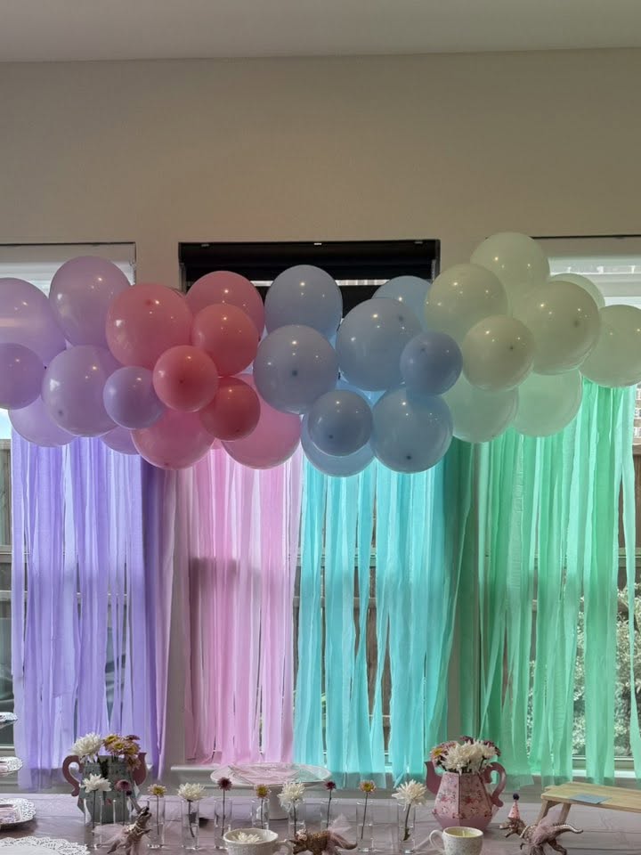Pastel balloon garland decoration with matching crepe paper streamers hanging against a window backdrop.