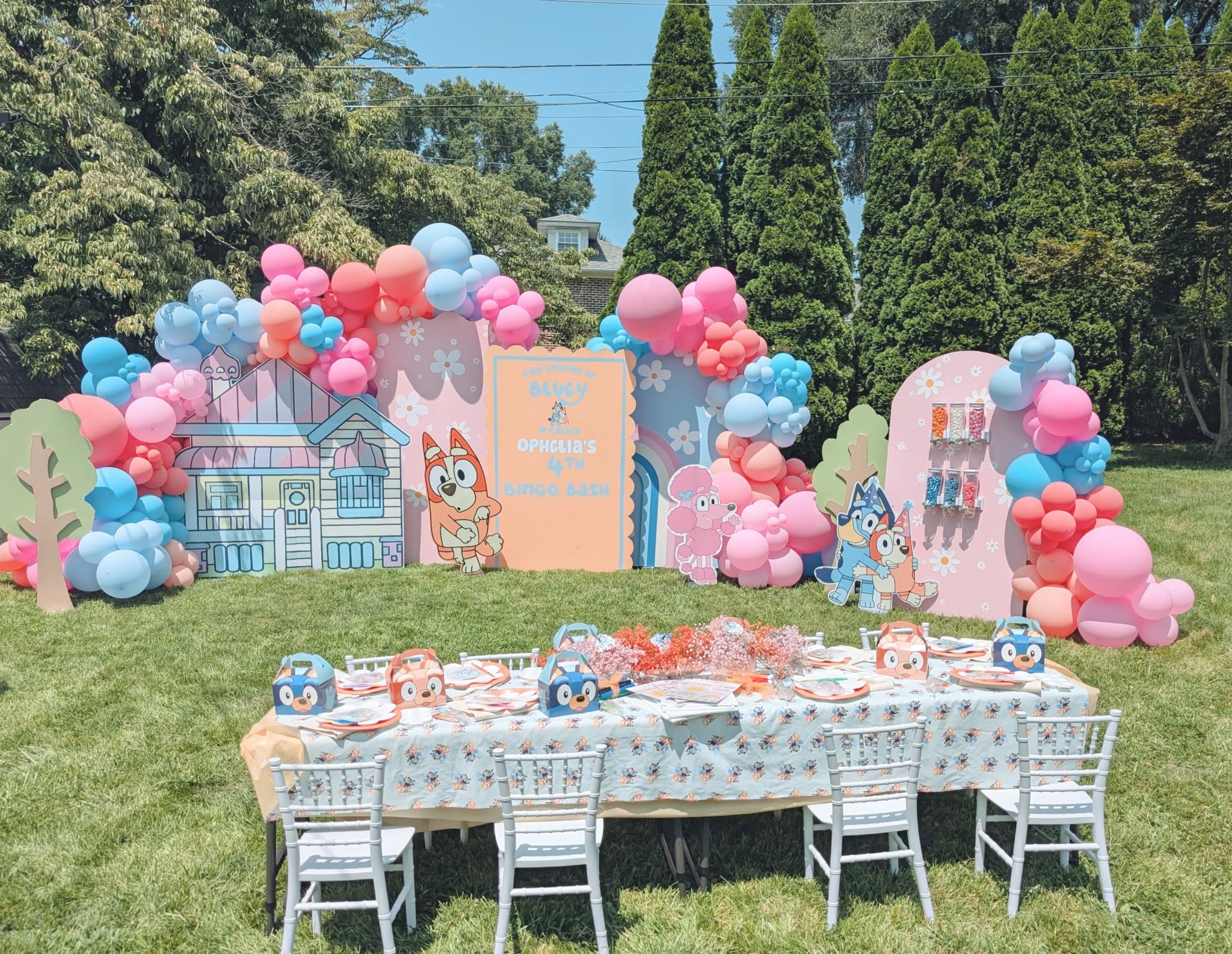Bluey-themed 4th birthday party setup in a backyard with balloon garland and table with Bluey party favor boxes.