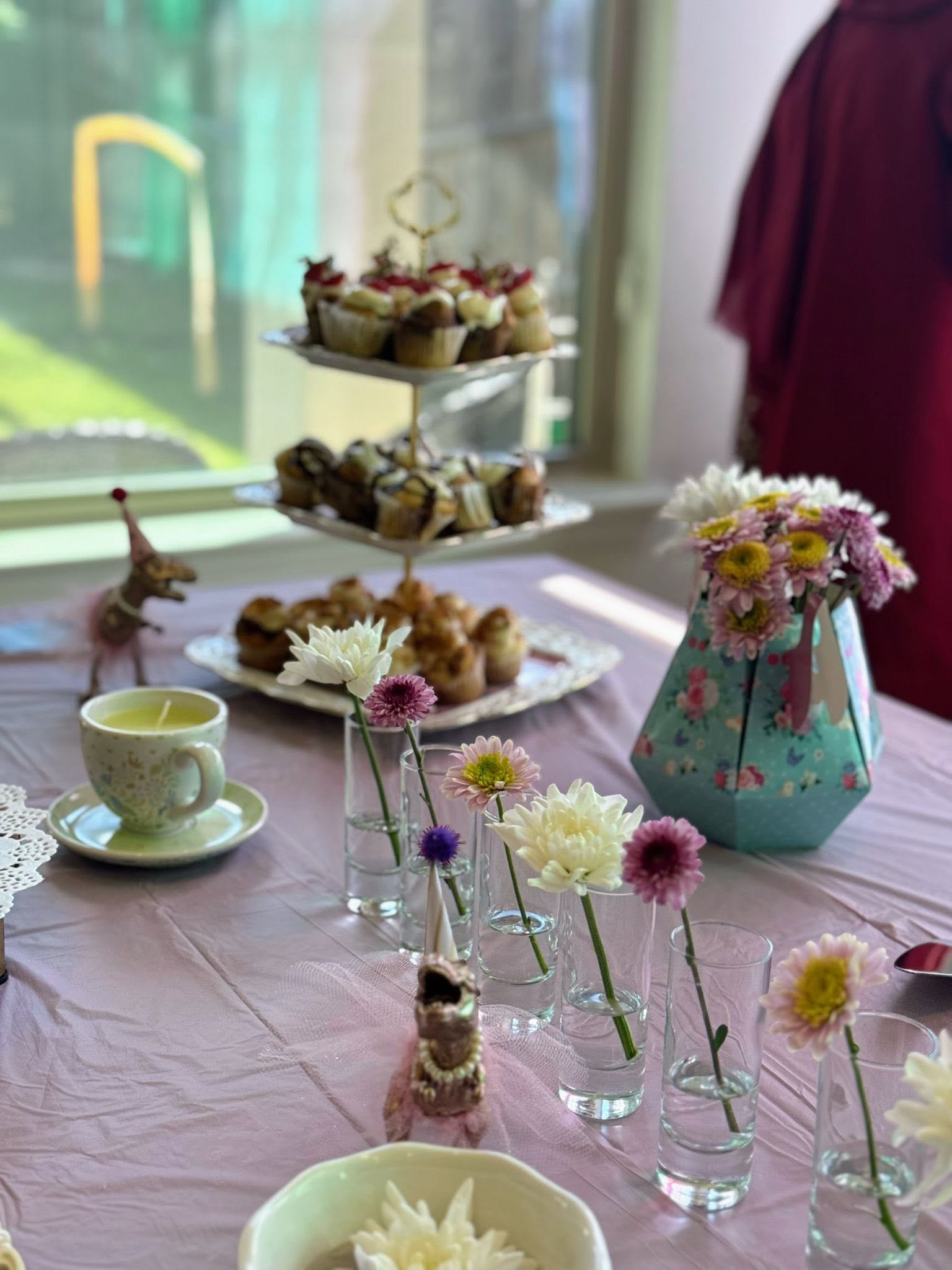 Tea party table setting with a three-tier cupcake stand, floral vases, and small dinosaur figurines.