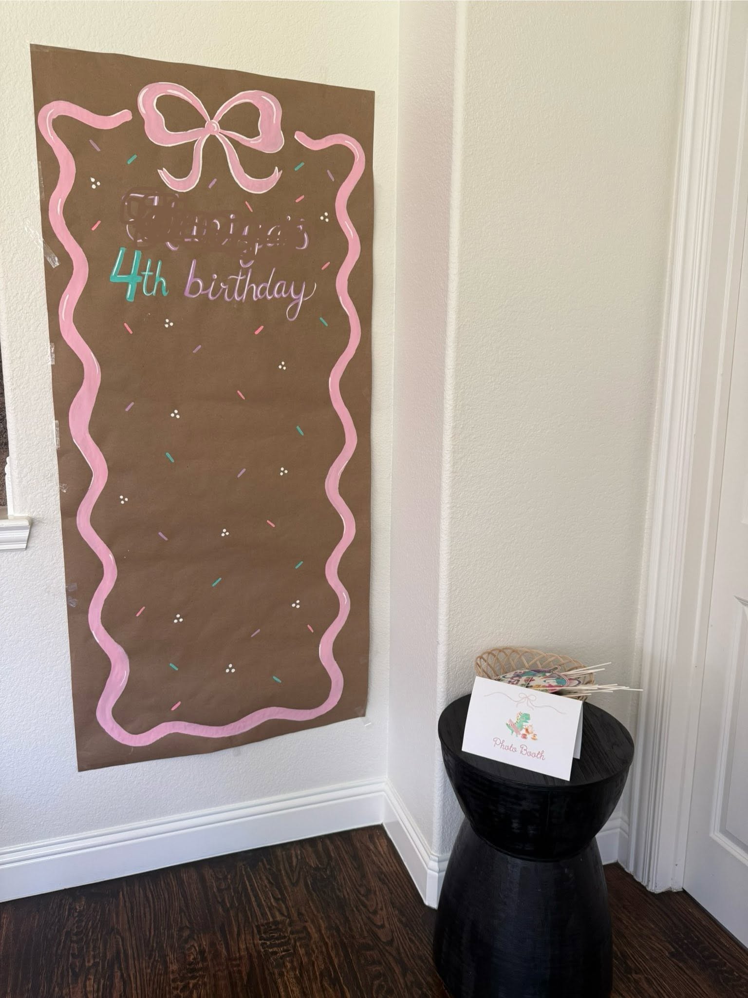 DIY 4th birthday photo booth backdrop with pink ribbon design and matching photo props on small side table
