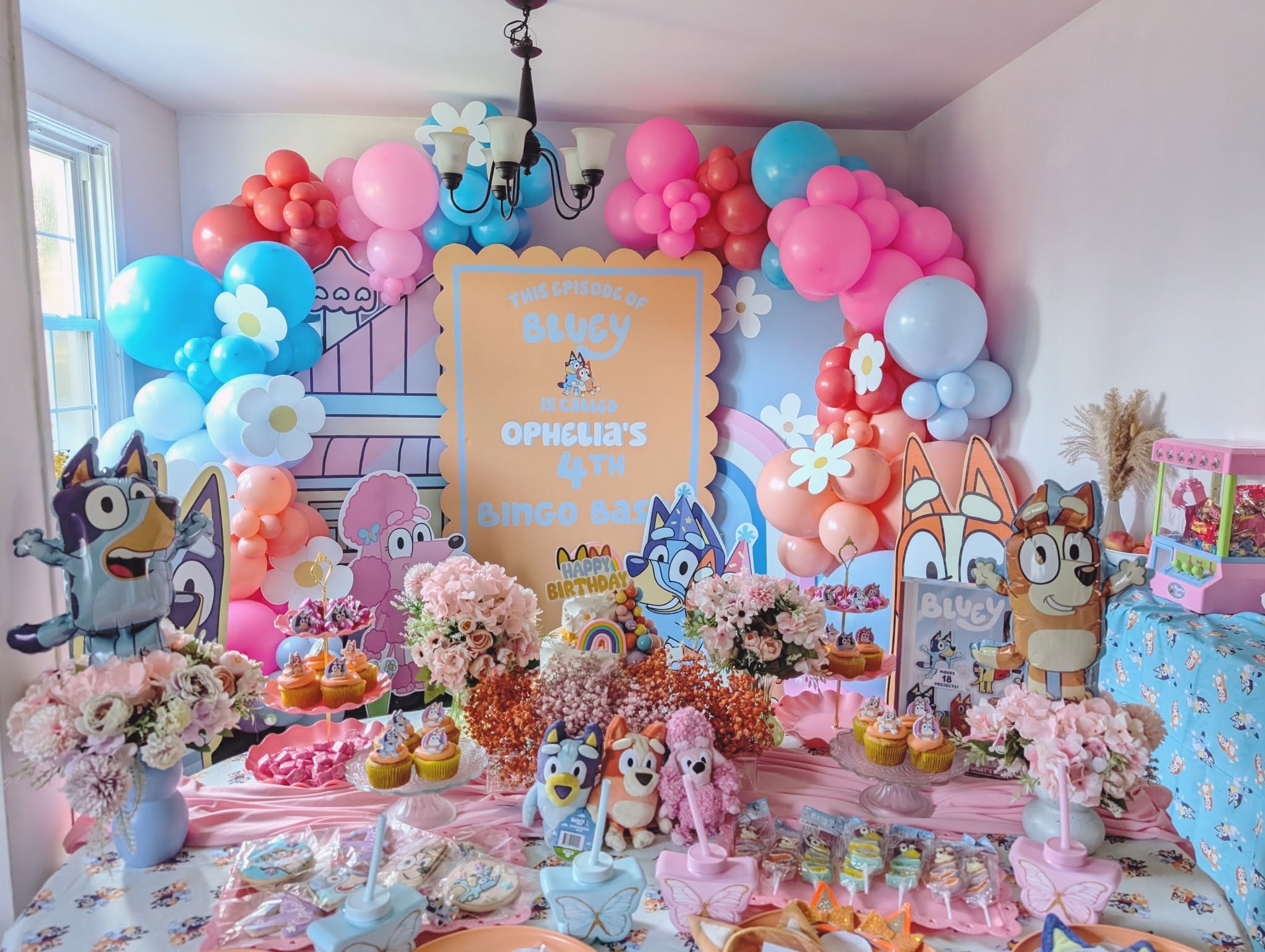 Bluey-themed birthday party dessert table with pastel balloons, character decorations, and cupcakes.
