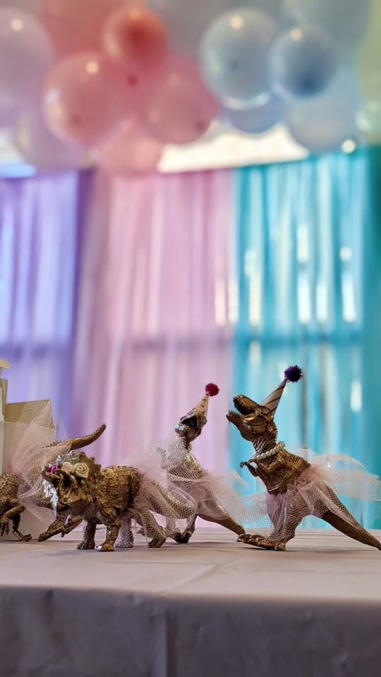 Gold toy dinosaurs dressed in pink tulle tutus and party hats as birthday party decorations.