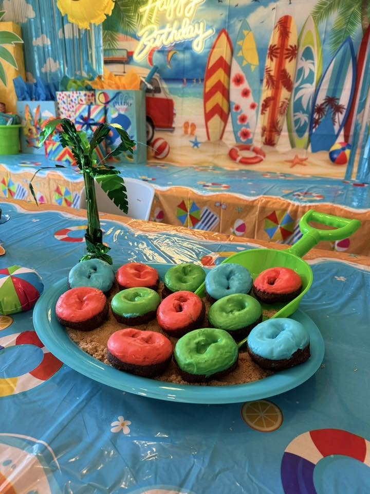 Platter of colorful frosted donuts served on a bed of cookie crumble sand at a beach-themed birthday party
