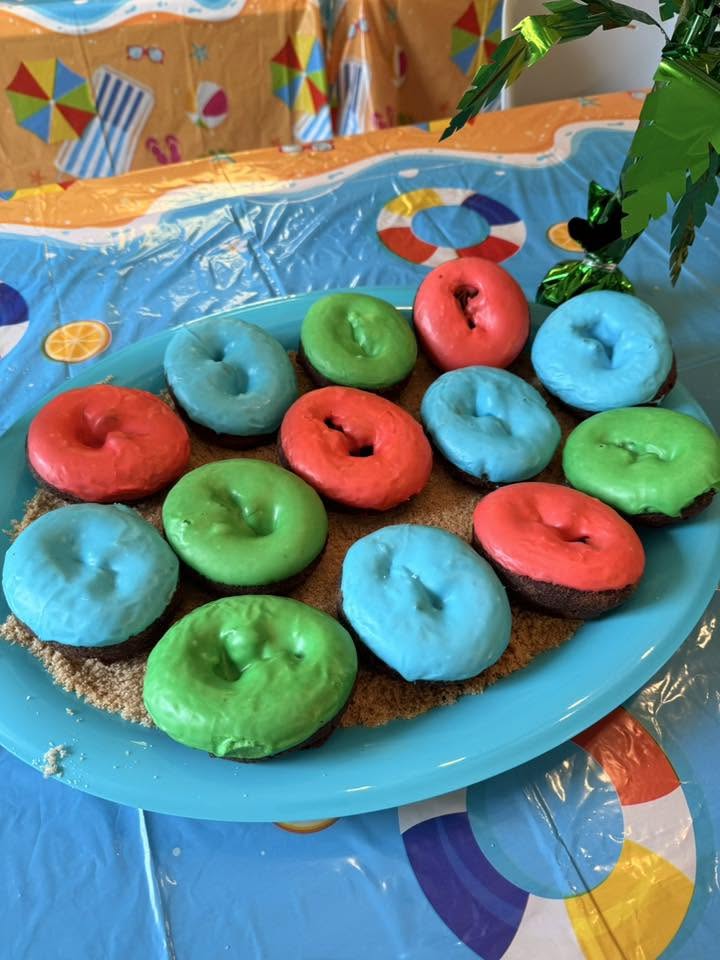 Donuts with bright blue, green, and red icing served on a tray of brown sugar for a beach-themed party.