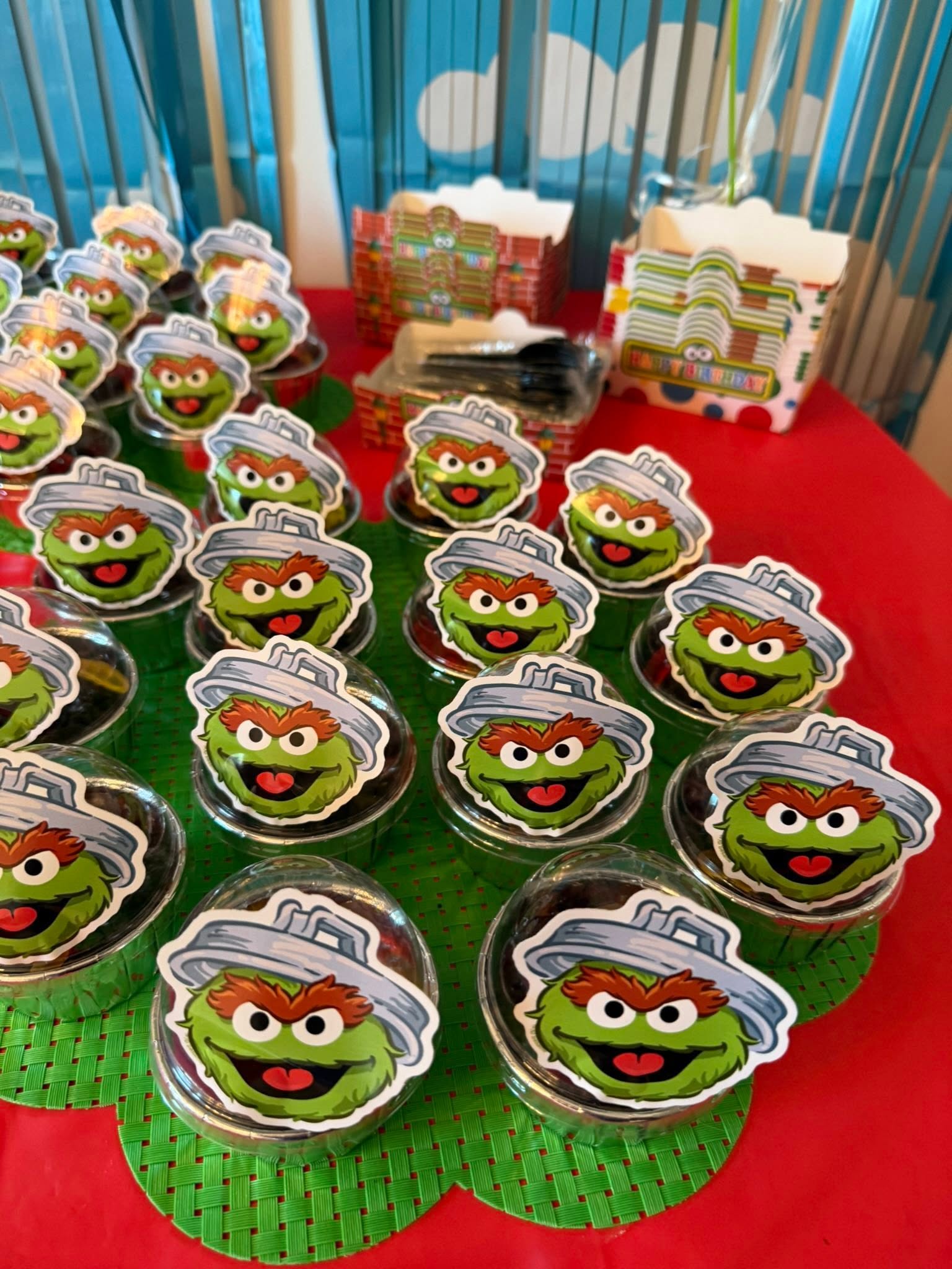 Table full of cupcake party favors decorated with Oscar the Grouch toppers inside clear plastic domes.