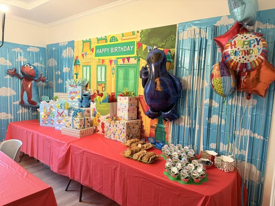 Sesame Street-themed birthday party setup with themed decorations, balloons, gifts, and treats on red tables
