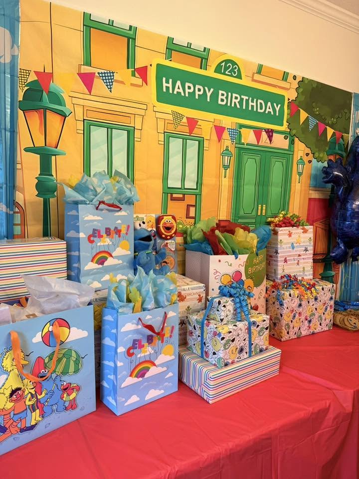 Sesame Street themed party backdrop with balloon-topped gift bags and wrapped presents on a red tablecloth