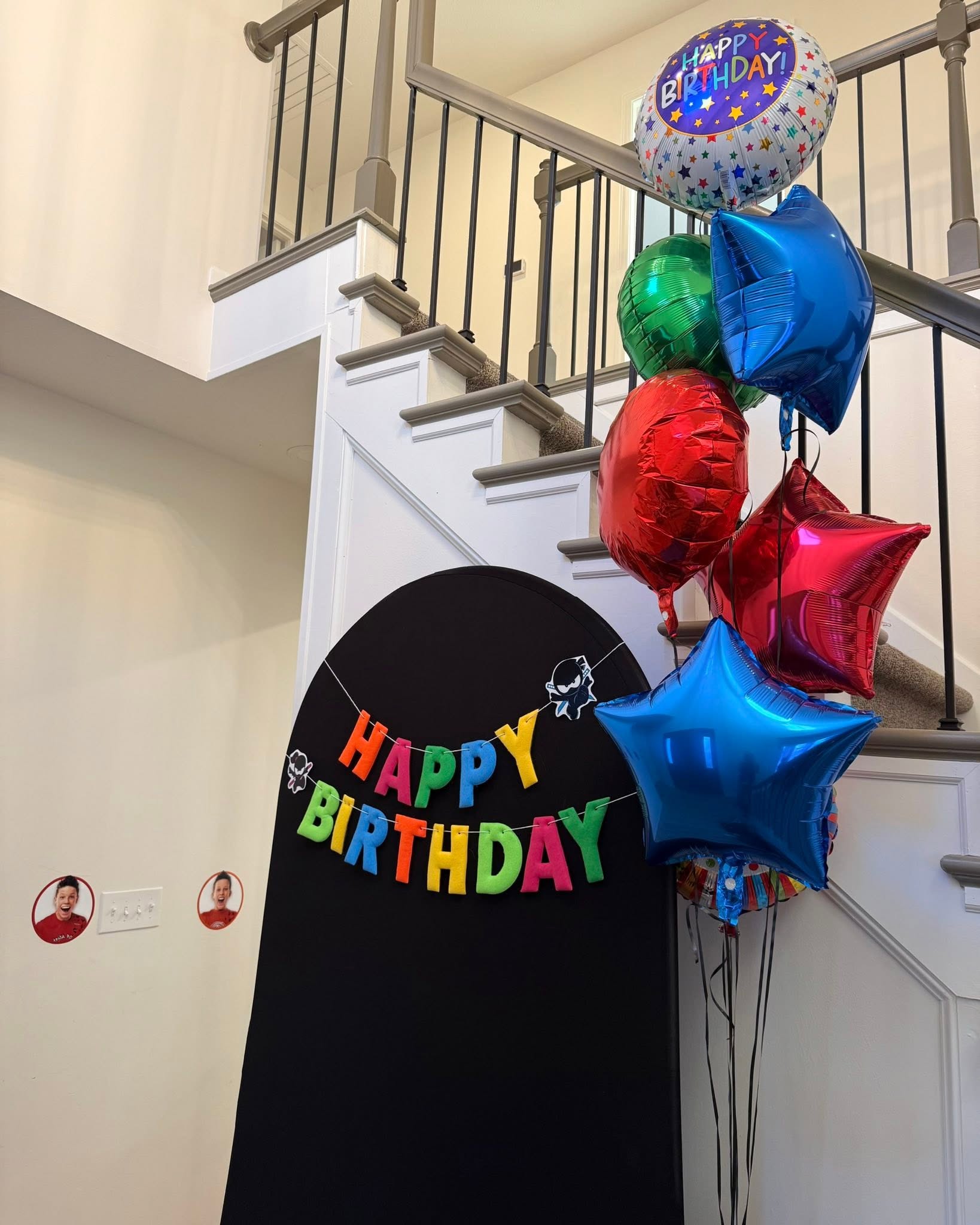 Colorful Happy Birthday banner on a black arch backdrop with a cluster of bright foil balloons